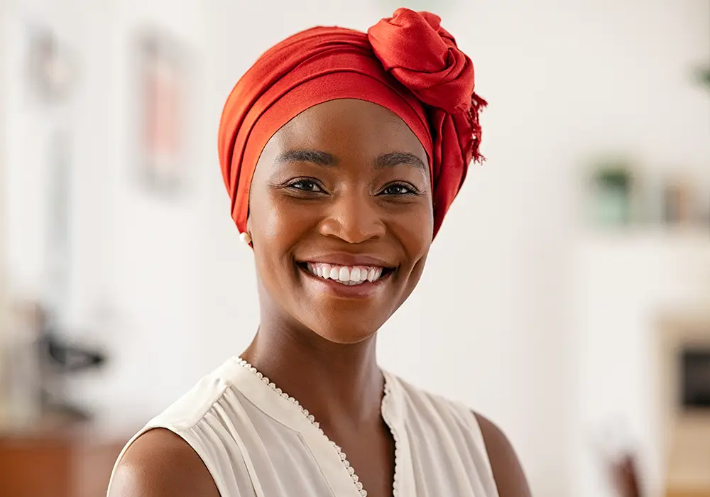 An african-american woman wearing a headscarf and smiling at the camera.