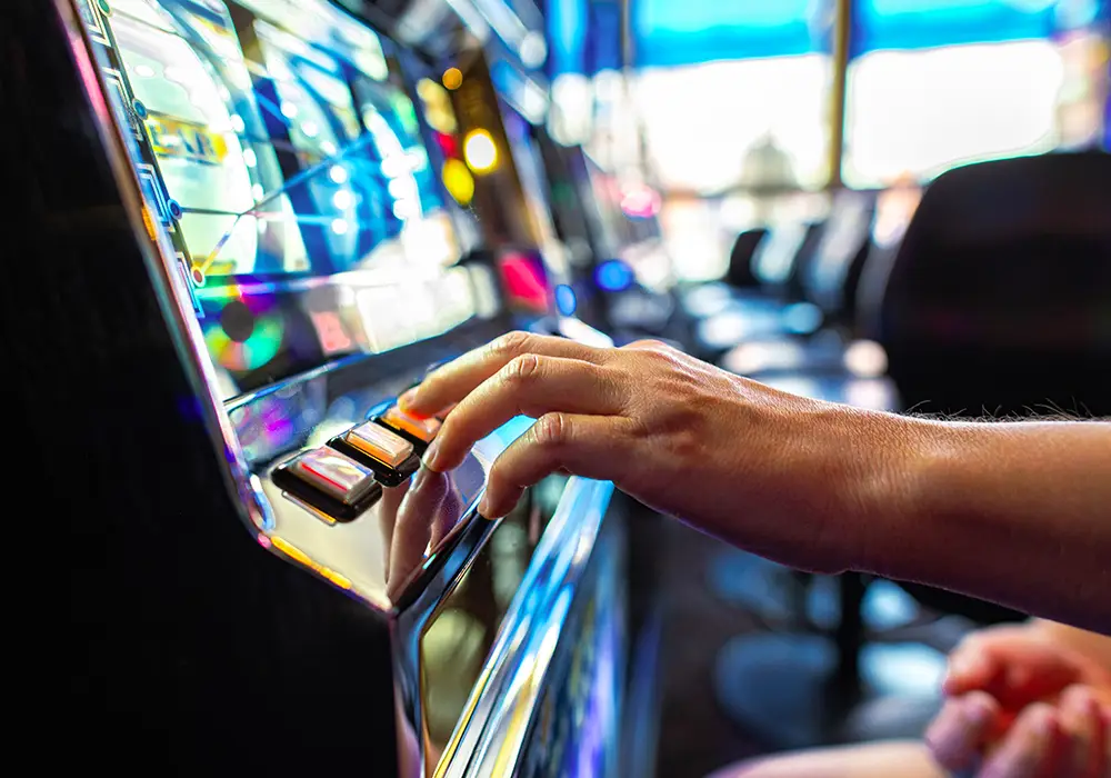 A closeup view of a man touching the buttons on an electronic slot machine.