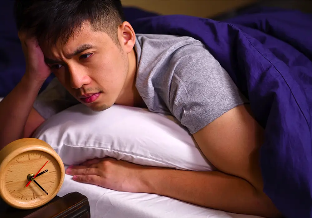 A distressed teenage boy staring at his alarm clock in bed.