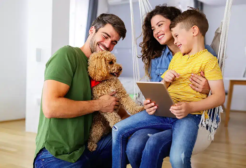 A family smiling and looking at a dog inside of a living room.